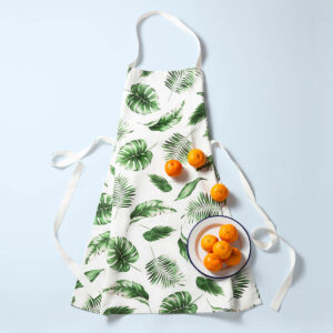 tropical leaf apron lying flat on the floor with a bowl of oranges